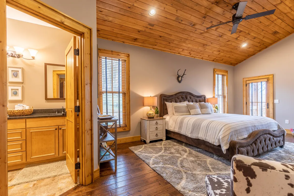 A serene bedroom featuring a plush bed, a vanity for getting ready, a cozy armchair by a large window, and abundant natural light streaming in. The setting feels restful and private, with a view that hints at tranquil mornings or quiet evenings.