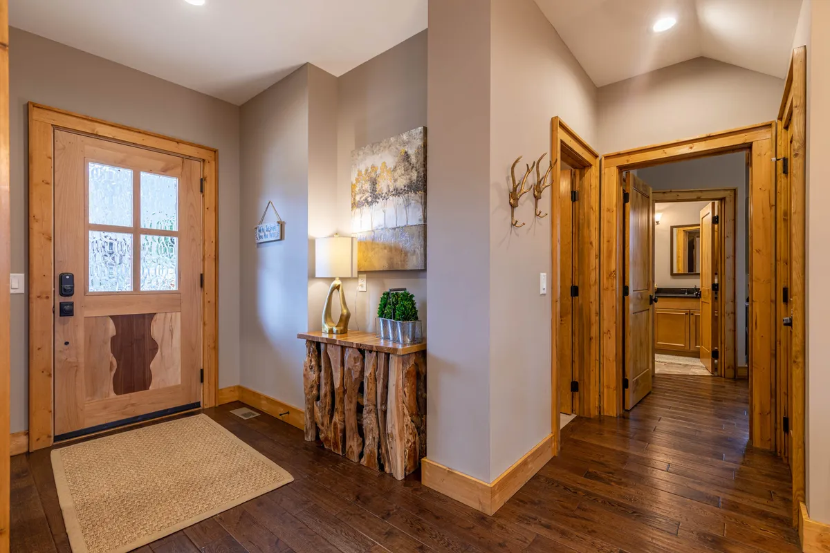 This photo shows a wooden front door entryway, styled with a console table, lamp, plant, and wall artwork. The area is warmly lit, creating an inviting first impression and a smooth transition from outside to inside.