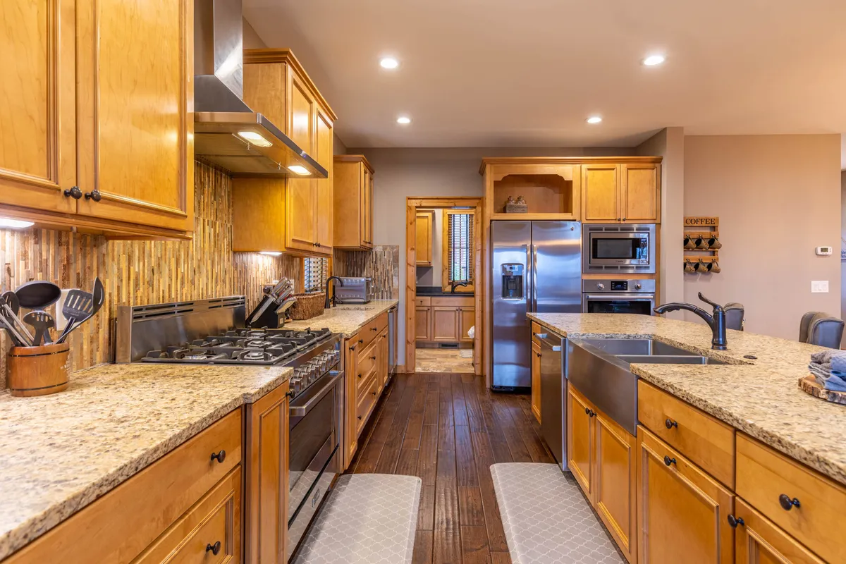 A bright and inviting kitchen featuring gleaming granite countertops, a spacious island with stools, stainless steel appliances, and warm wood cabinetry. The space is open and perfect for both meal preparation and socializing, with clear sightlines to adjacent living areas.