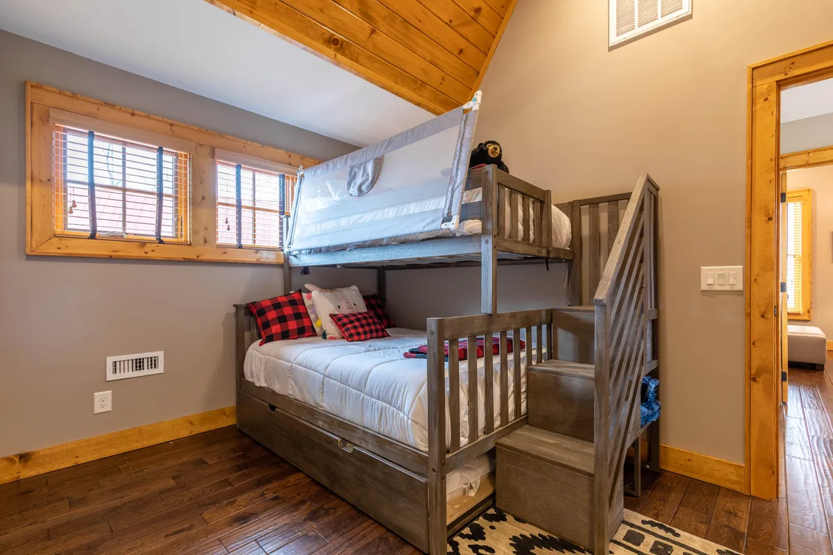 A playful, well-lit bunk room with cheerful plaid pillows, wooden accents, and cozy bedding. The environment is tailored for kids or groups, providing a warm, inviting space for sleep and bonding.