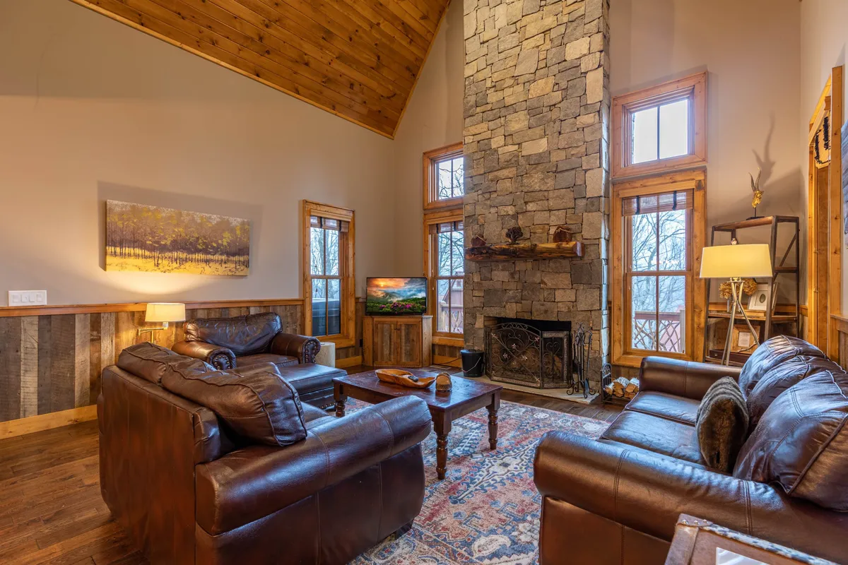 A welcoming living room with plush leather sofas arranged around a striking stone fireplace, large windows letting in natural light, and wooden accents that add rustic charm. The setting is cozy, perfect for relaxing or streaming a favorite movie after a day outdoors.