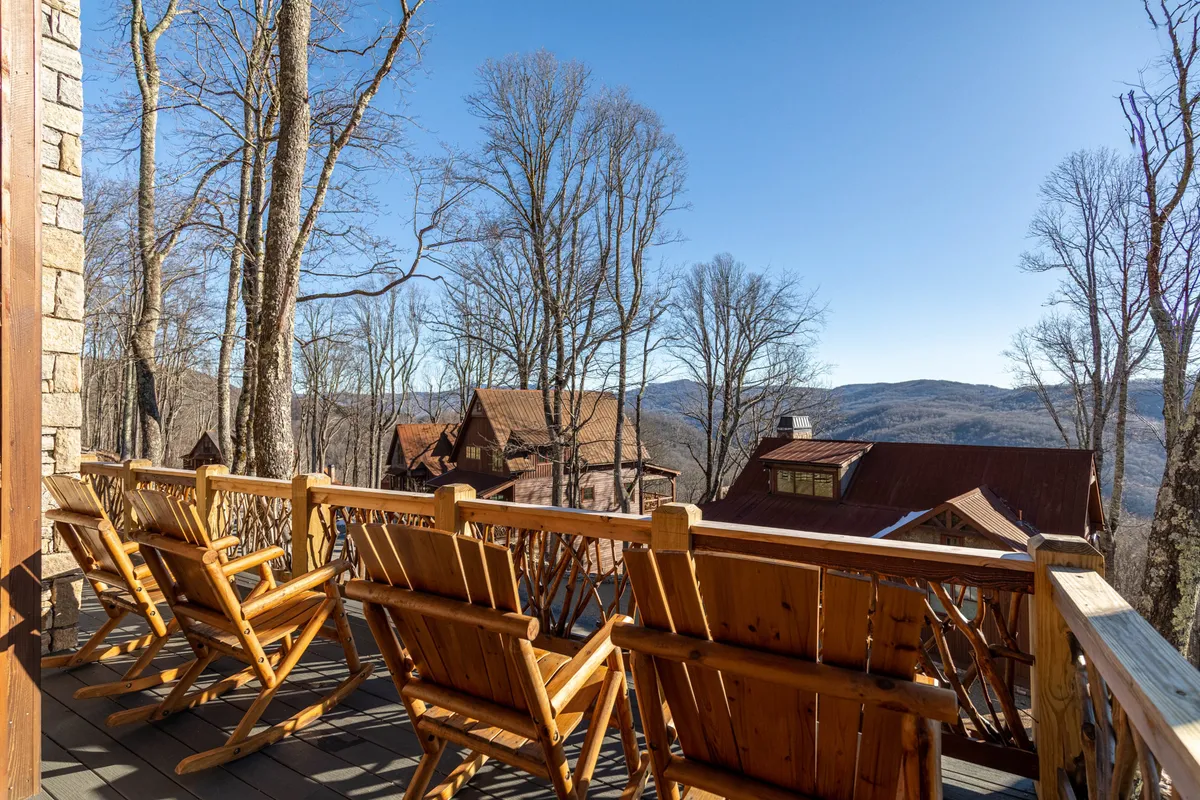 A peaceful exterior setting with wooden chairs positioned for mountain and tree views, adjacent to neighboring cabins. The scene suggests relaxing after a day of activities, watching sunset or wildlife, and bonding with family in nature's embrace.