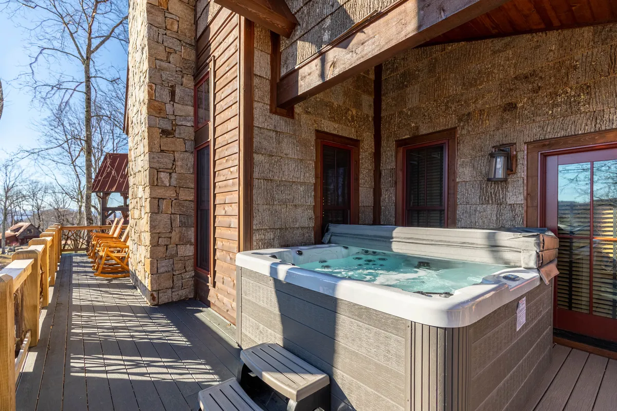 This image showcases a wooden deck with a hot tub, bordered by a stone wall and featuring warm red doors. The setup is inviting, with the hot tub positioned to overlook the outdoor scenery, emphasizing a tranquil space for relaxation and socializing.